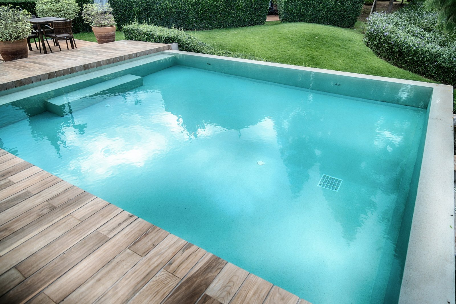 Outdoor swimming pool bordered by a wood deck and garden